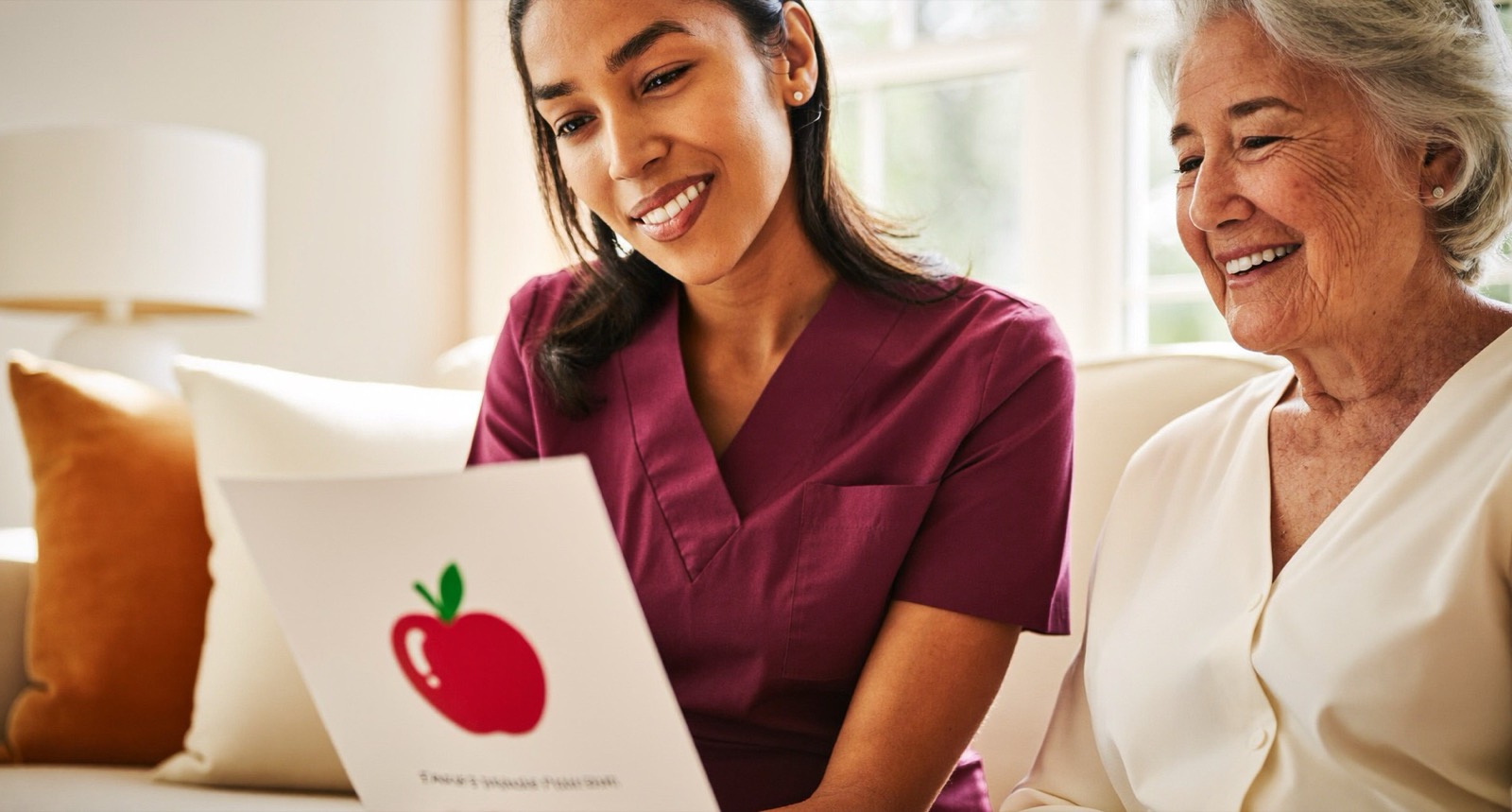 A speech-language pathologist holding a picture flashcard for a senior woman on her sofa